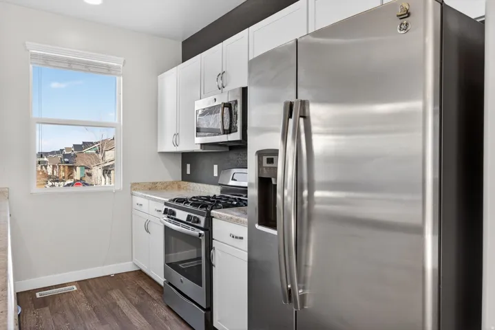 Kitchen with stainless steel appliances, white cabinets, and dark wood-style floors