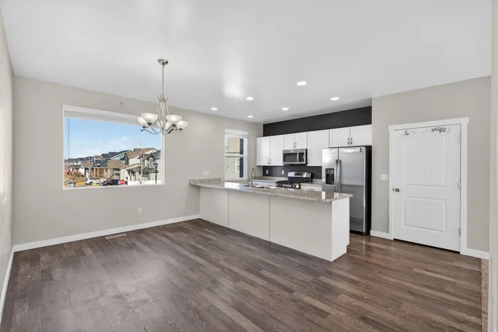 Kitchen with stainless steel appliances, a peninsula, white cabinetry, hanging lights, and light stone counters
