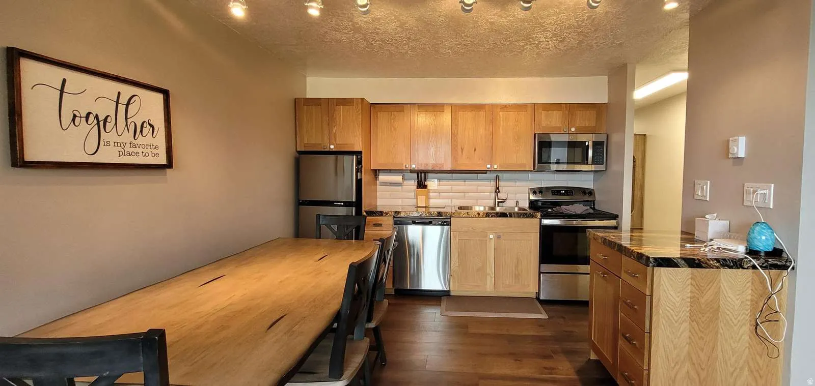Kitchen with stainless steel appliances, dark wood-type flooring, backsplash, a textured ceiling, and wood finish cabinetry