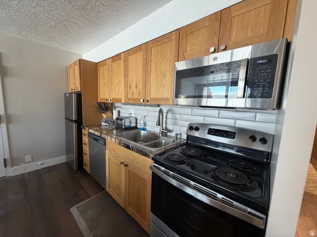 Kitchen with stainless steel appliances, backsplash, a textured ceiling, dark wood-style floors, and dark countertops