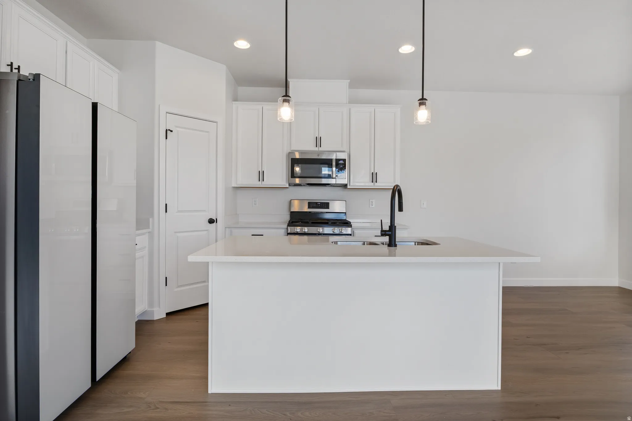 Kitchen with stainless steel appliances, hanging light fixtures, dark wood-type flooring, white cabinets, and a kitchen island with sink