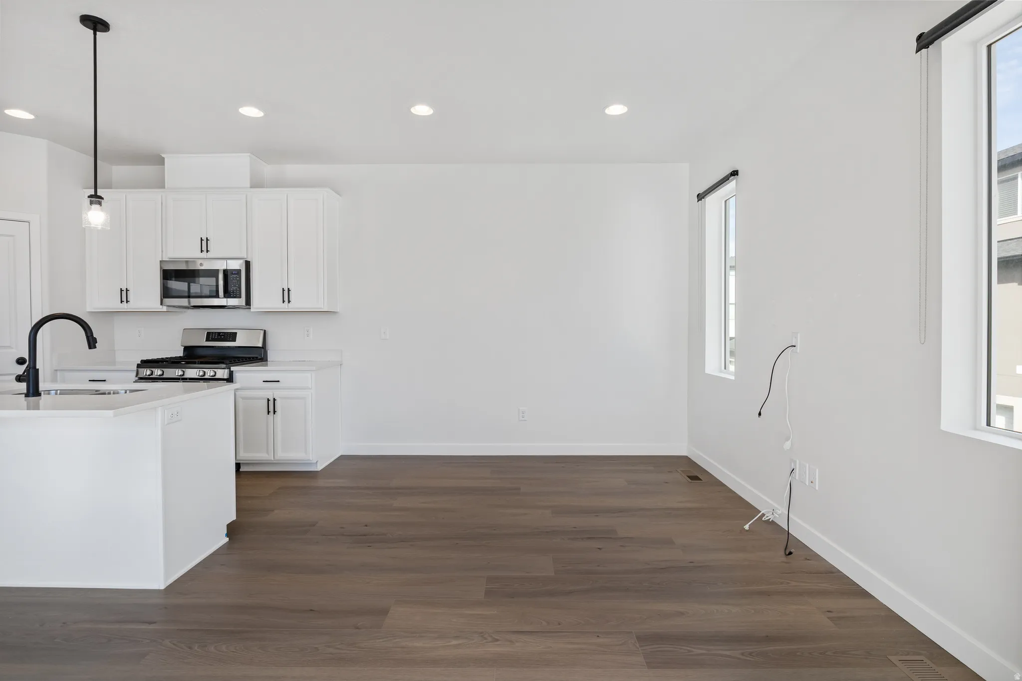 Kitchen with white cabinetry, dark wood-style flooring, stainless steel appliances, hanging light fixtures, and plenty of natural light