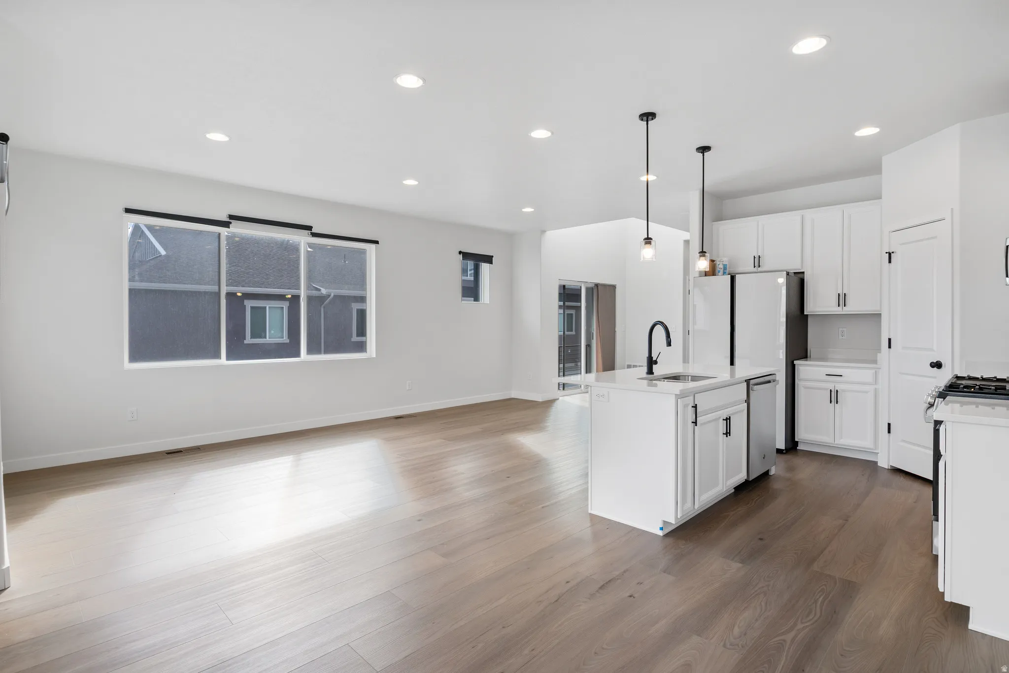 Kitchen featuring an island with sink, open floor plan, white cabinetry, decorative light fixtures, and dark wood-type flooring