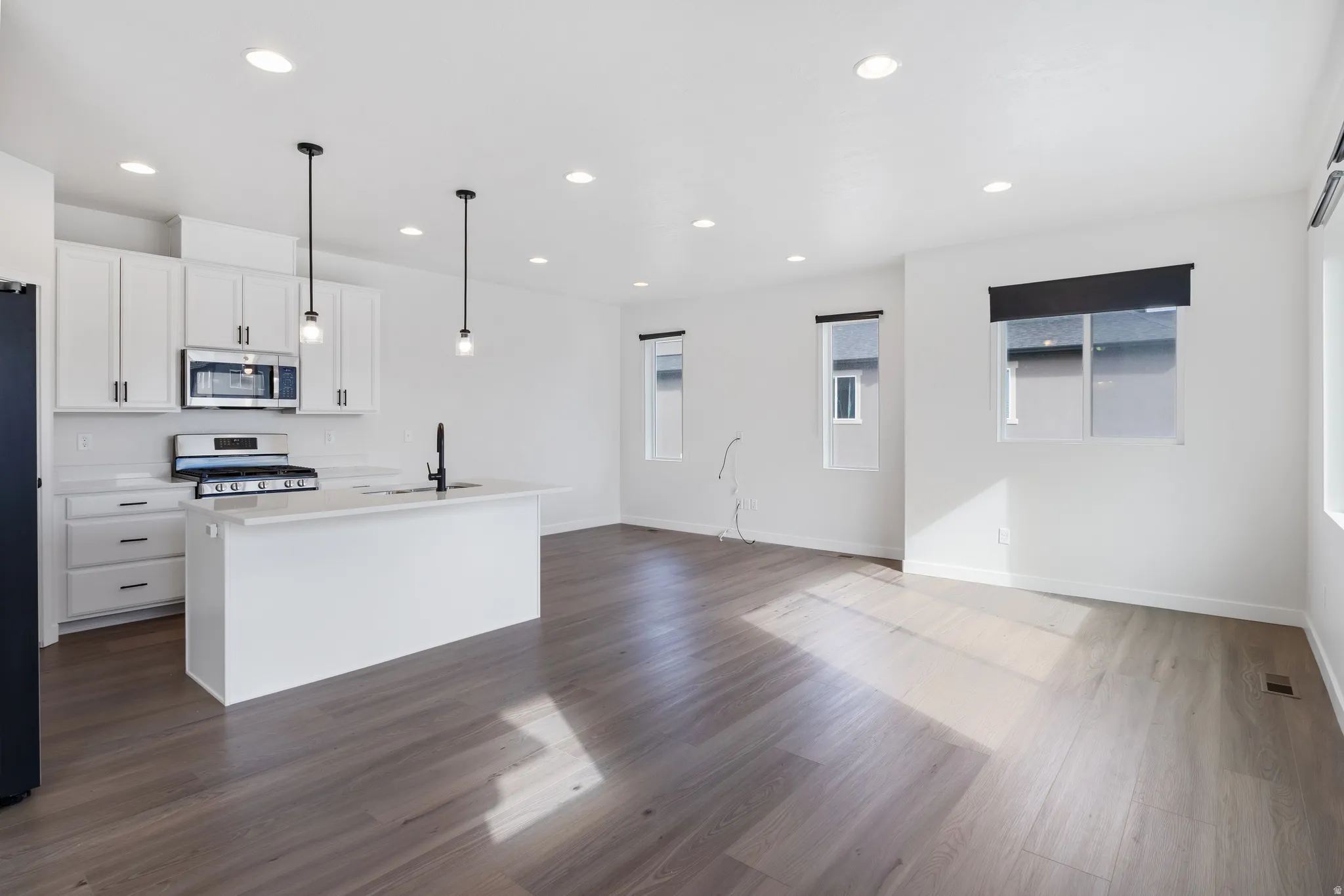 Kitchen with stainless steel appliances, white cabinetry, a center island with sink, open floor plan, and pendant lighting