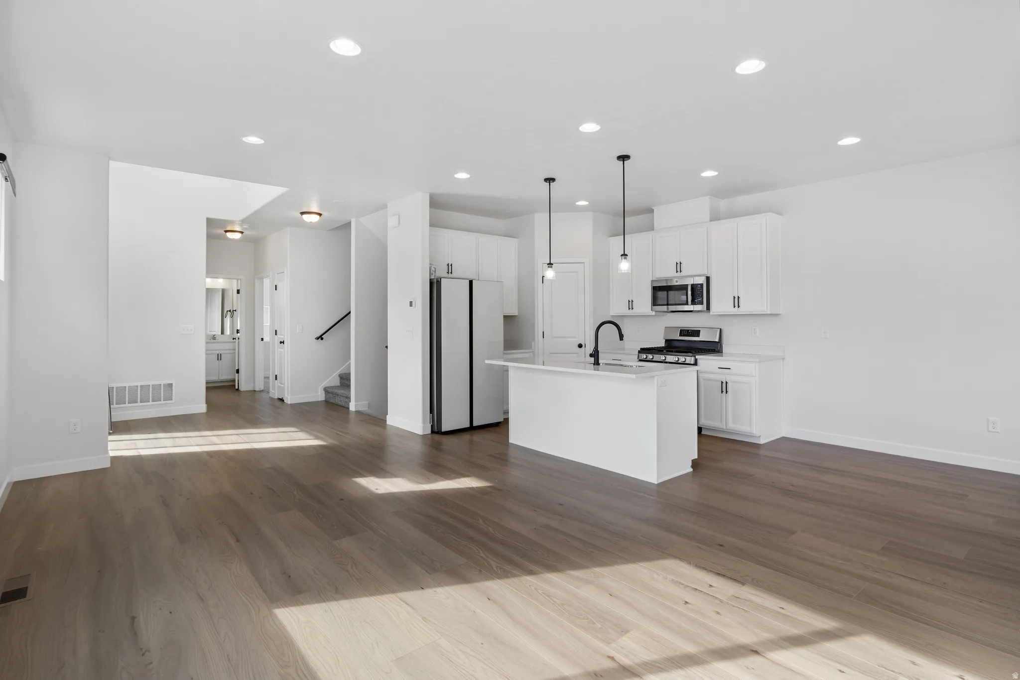 Kitchen featuring open floor plan, white cabinets, stainless steel appliances, and dark wood-style floors