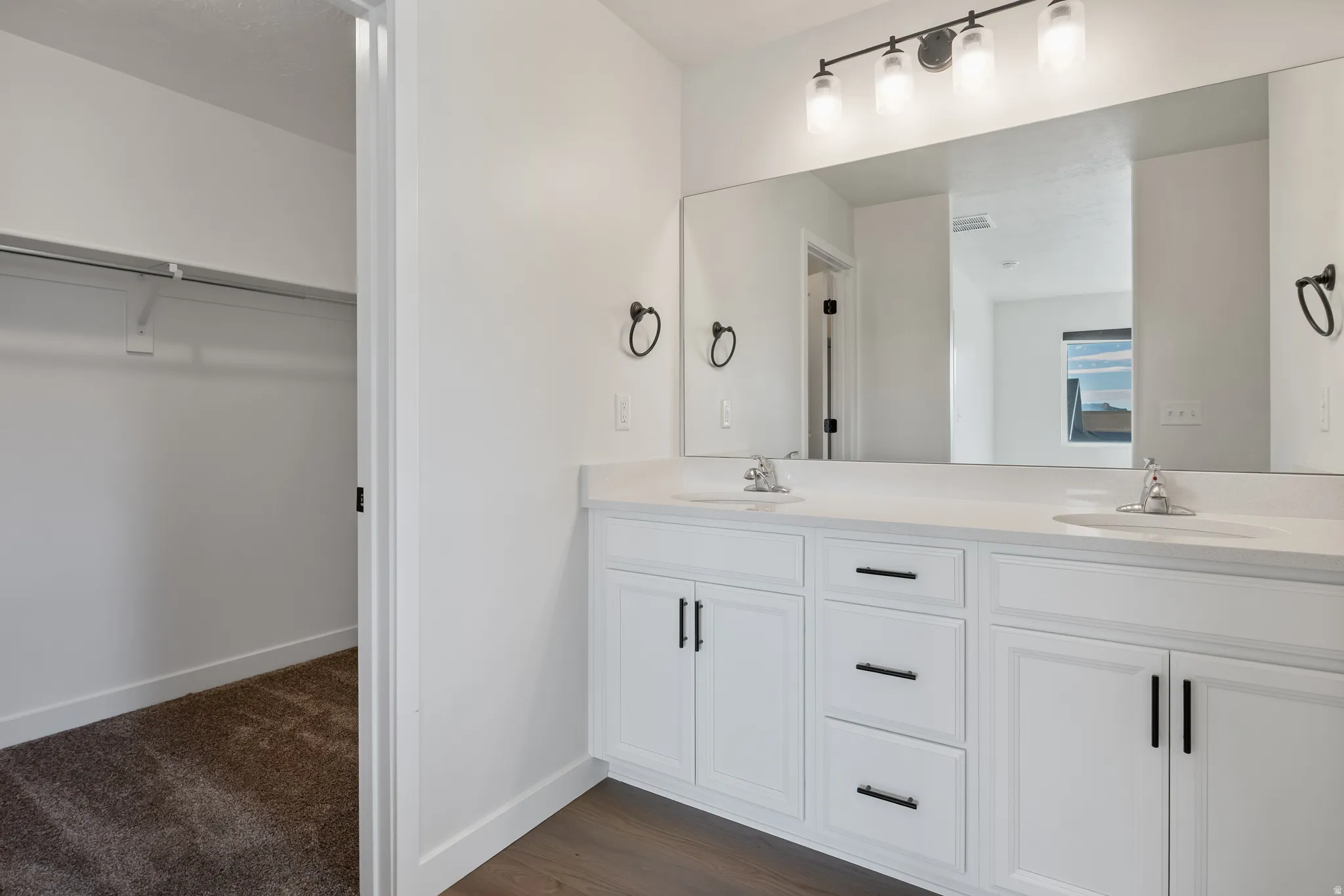 Full bath featuring double vanity, a spacious closet, and dark wood-style floors