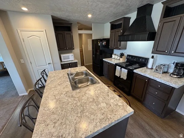 Kitchen featuring black appliances, light countertops, a kitchen island with sink, a kitchen bar, and dark wood finish cabinets