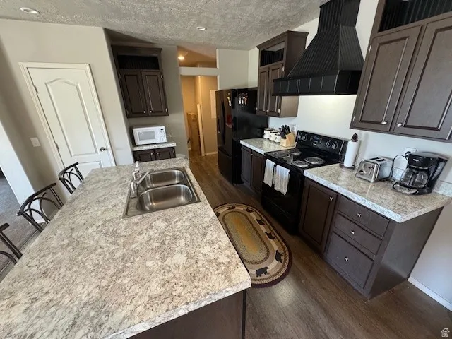 Kitchen with dark wood-type flooring, a kitchen breakfast bar, light countertops, dark wood finish cabinets, and a textured ceiling
