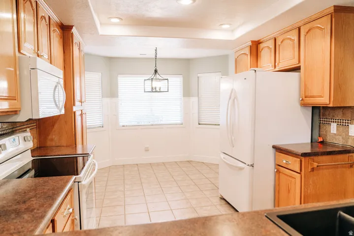 Kitchen featuring white appliances, dark countertops, backsplash, a wainscoted wall, and hanging light fixtures