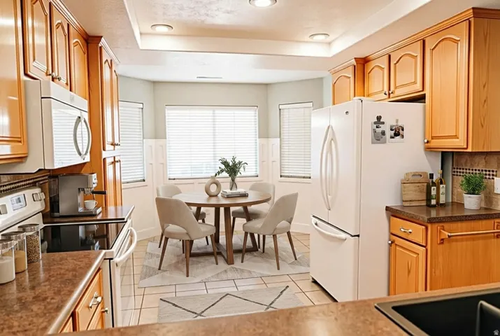 Kitchen featuring white appliances, dark countertops, tasteful backsplash, a tray ceiling, and light tile patterned flooring