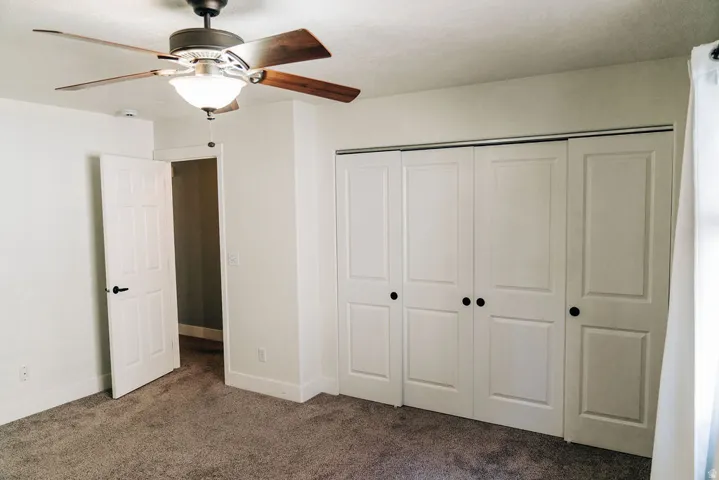 Unfurnished bedroom with dark carpet, a ceiling fan, and a closet
