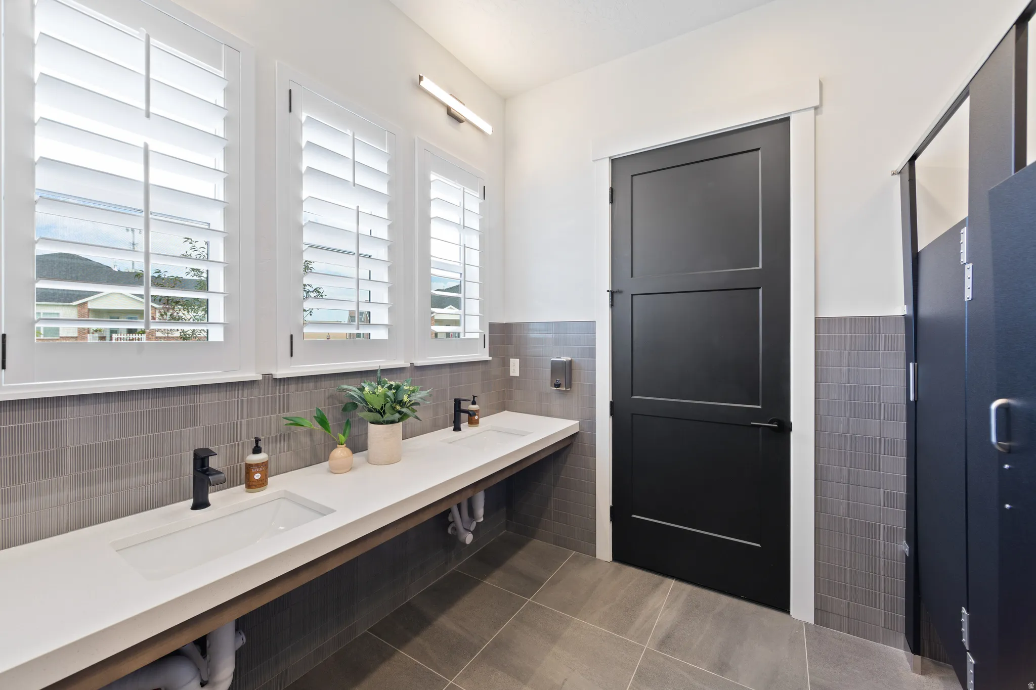 Full bath featuring double vanity, dark tile patterned flooring, tile walls, and wainscoting
