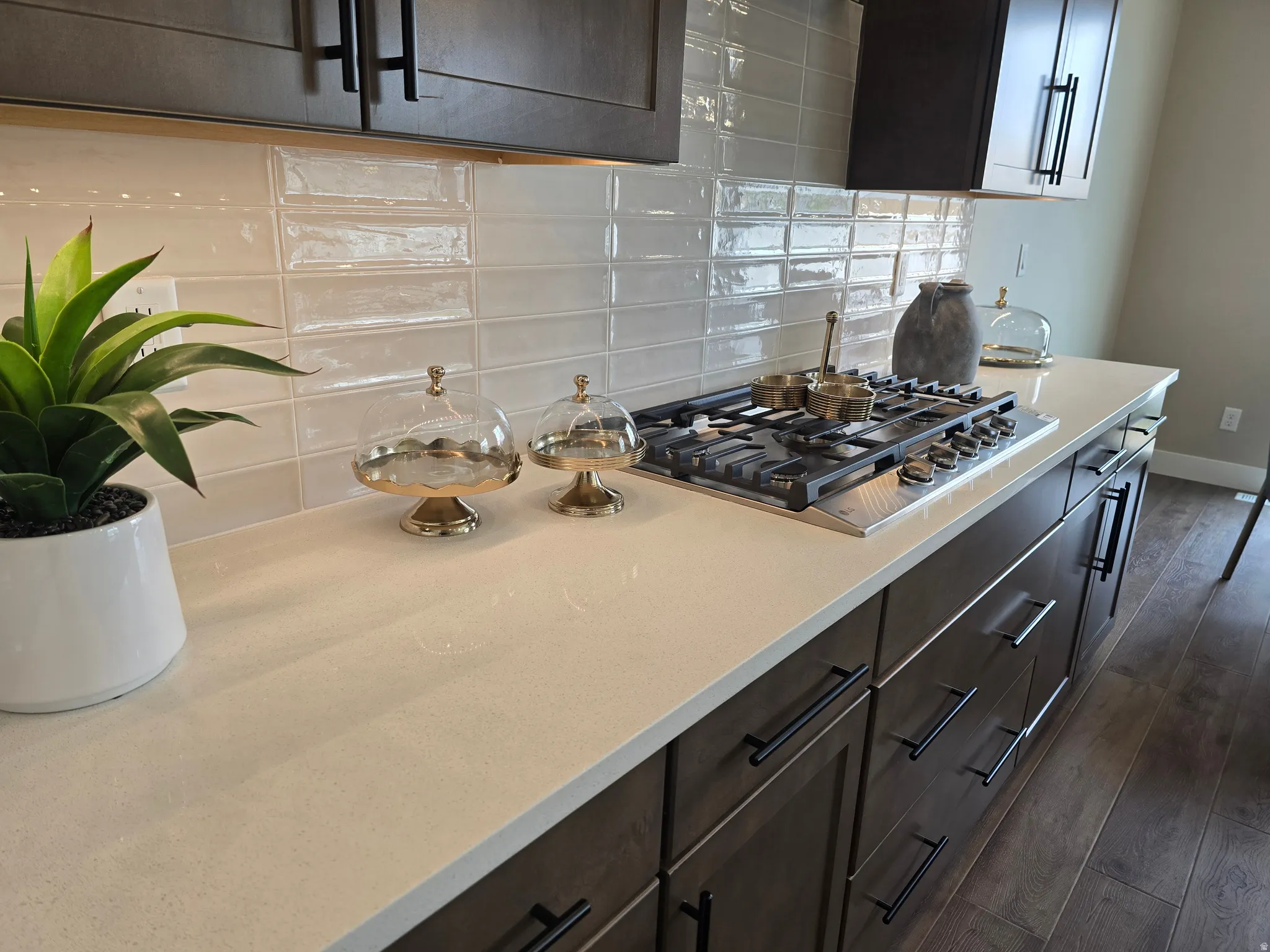 Kitchen featuring dark wood finish cabinetry, backsplash, light stone countertops, dark wood-style flooring, and stainless steel gas cooktop