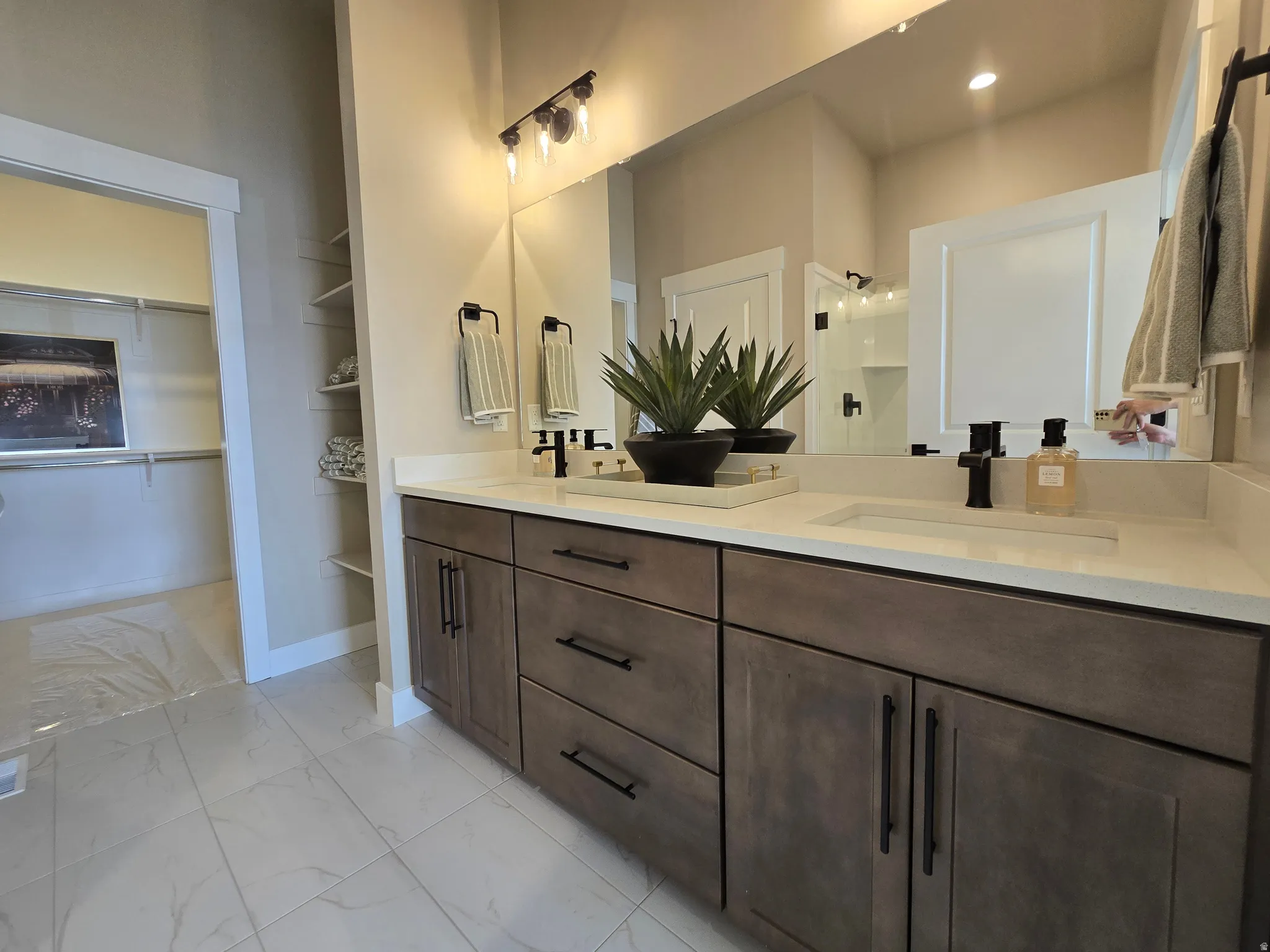 Full bath featuring double vanity, light marble finish flooring, a spacious closet, and a shower