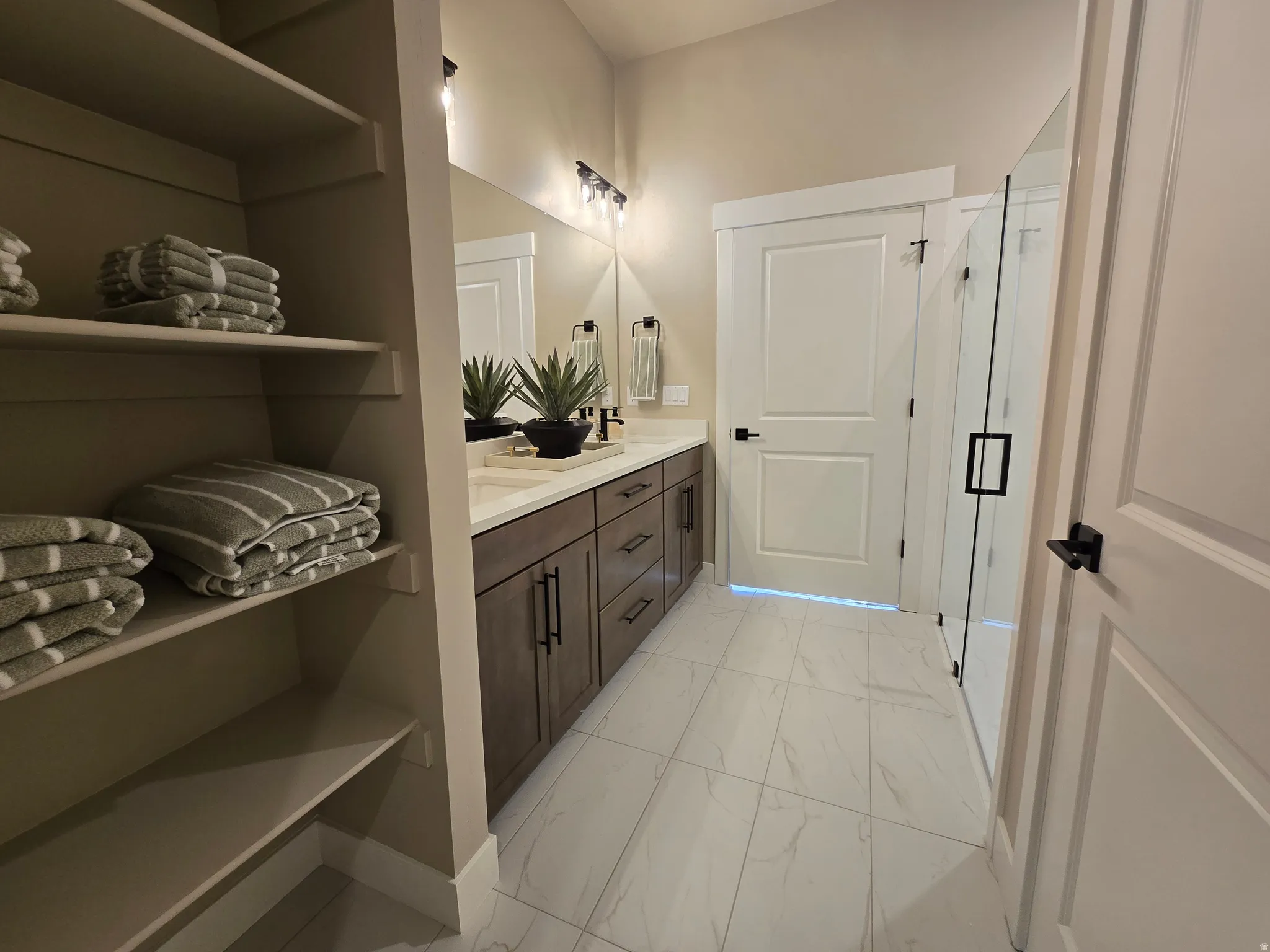 Bathroom with double vanity, light marble finish flooring, and a stall shower