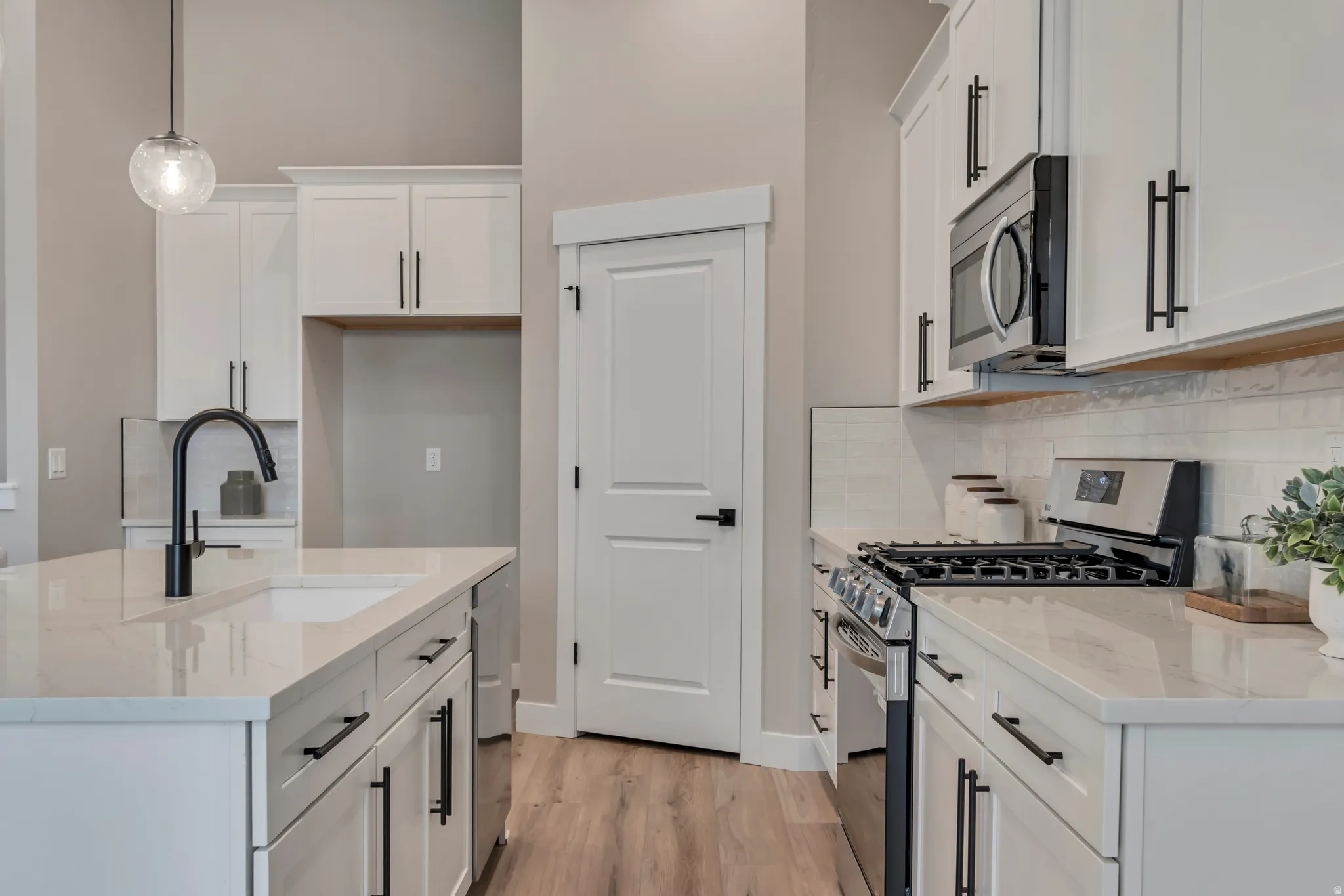 Kitchen with stainless steel appliances, light stone countertops, white cabinets, and decorative light fixtures