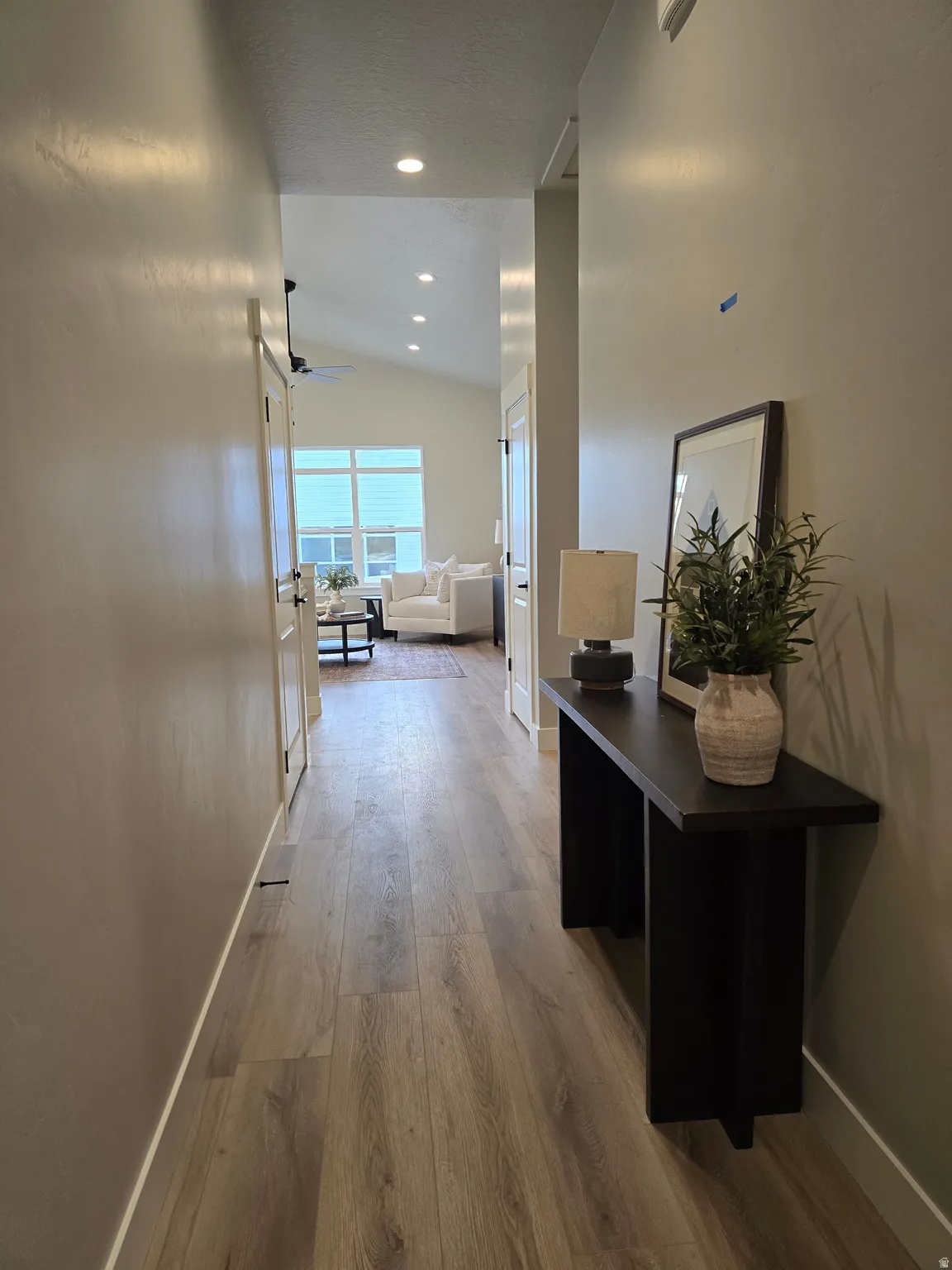 Hallway with light wood-style flooring, lofted ceiling, and recessed lighting