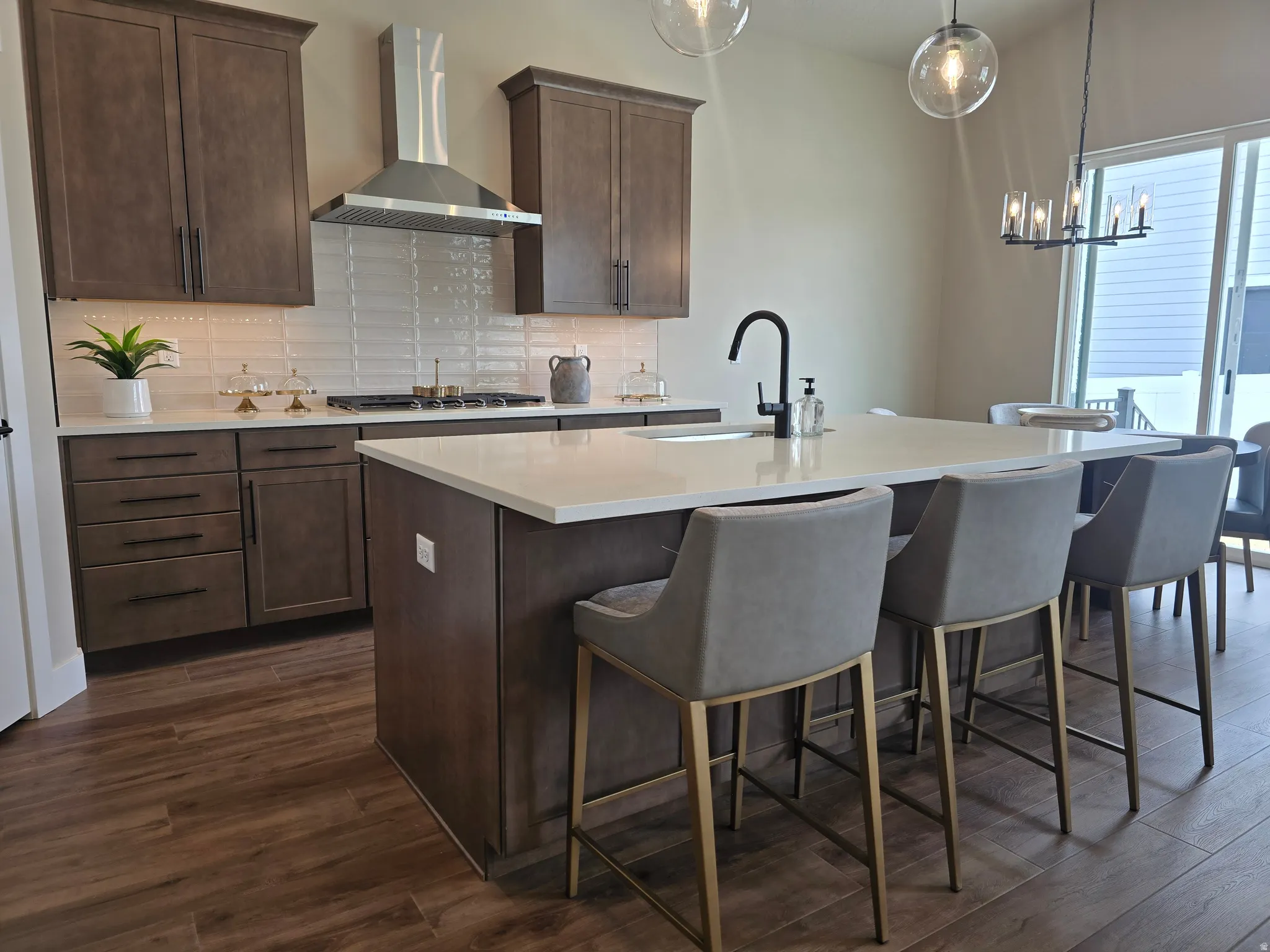 Kitchen featuring dark wood finished floors, dark wood finish cabinets, an island with sink, decorative backsplash, and a kitchen bar