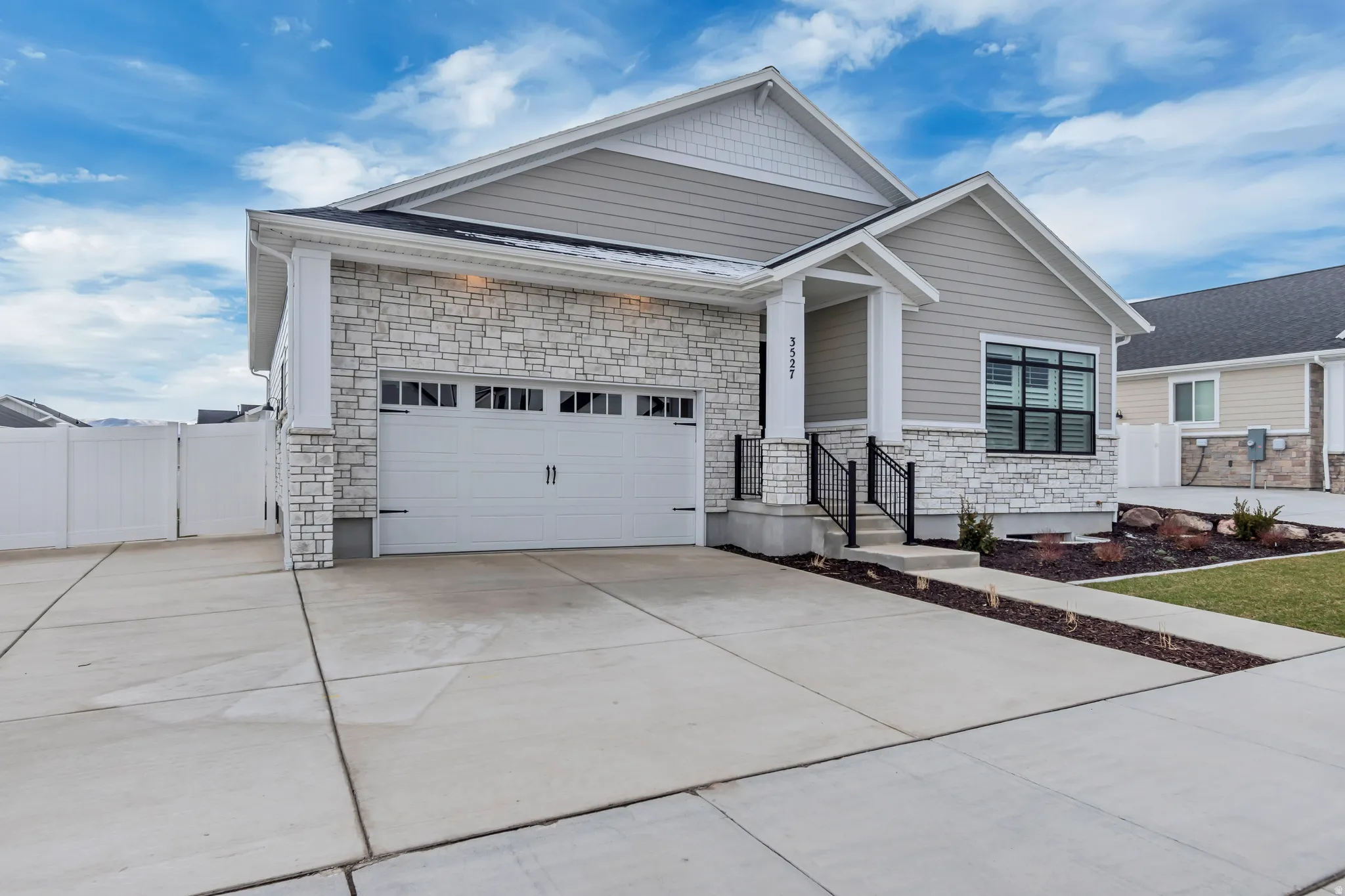 View of front of property featuring stone siding, driveway, an attached garage, and a gate