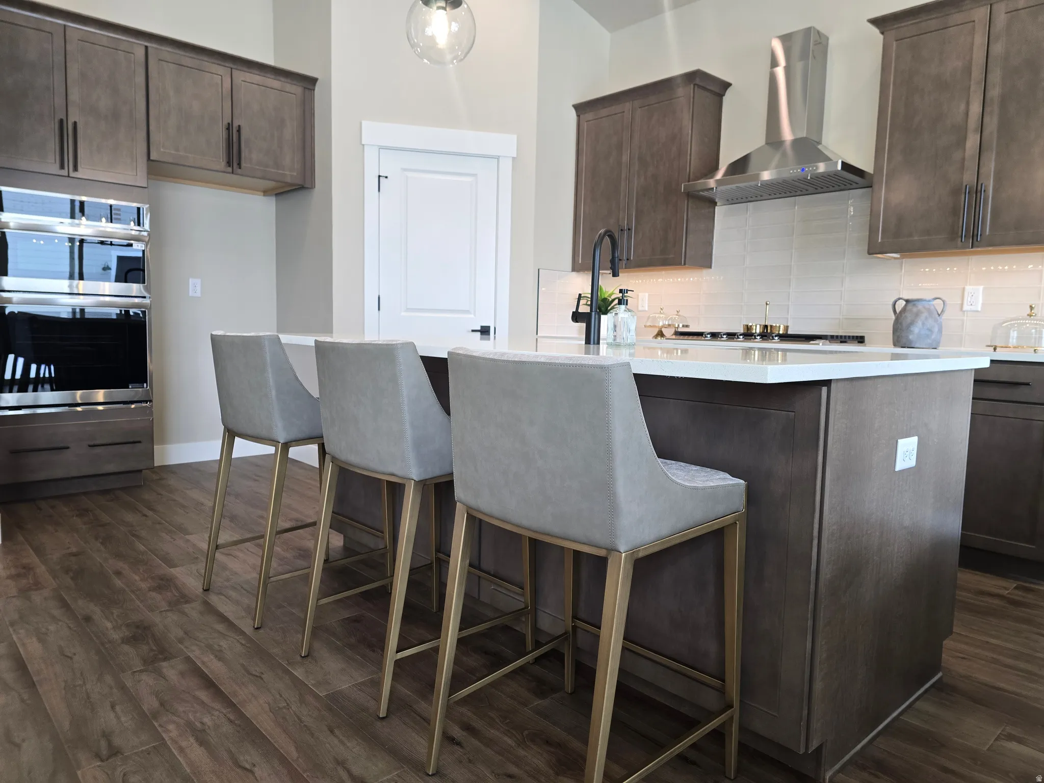 Kitchen with dark wood finish cabinetry, an island with sink, double oven, dark wood-style floors, and tasteful backsplash
