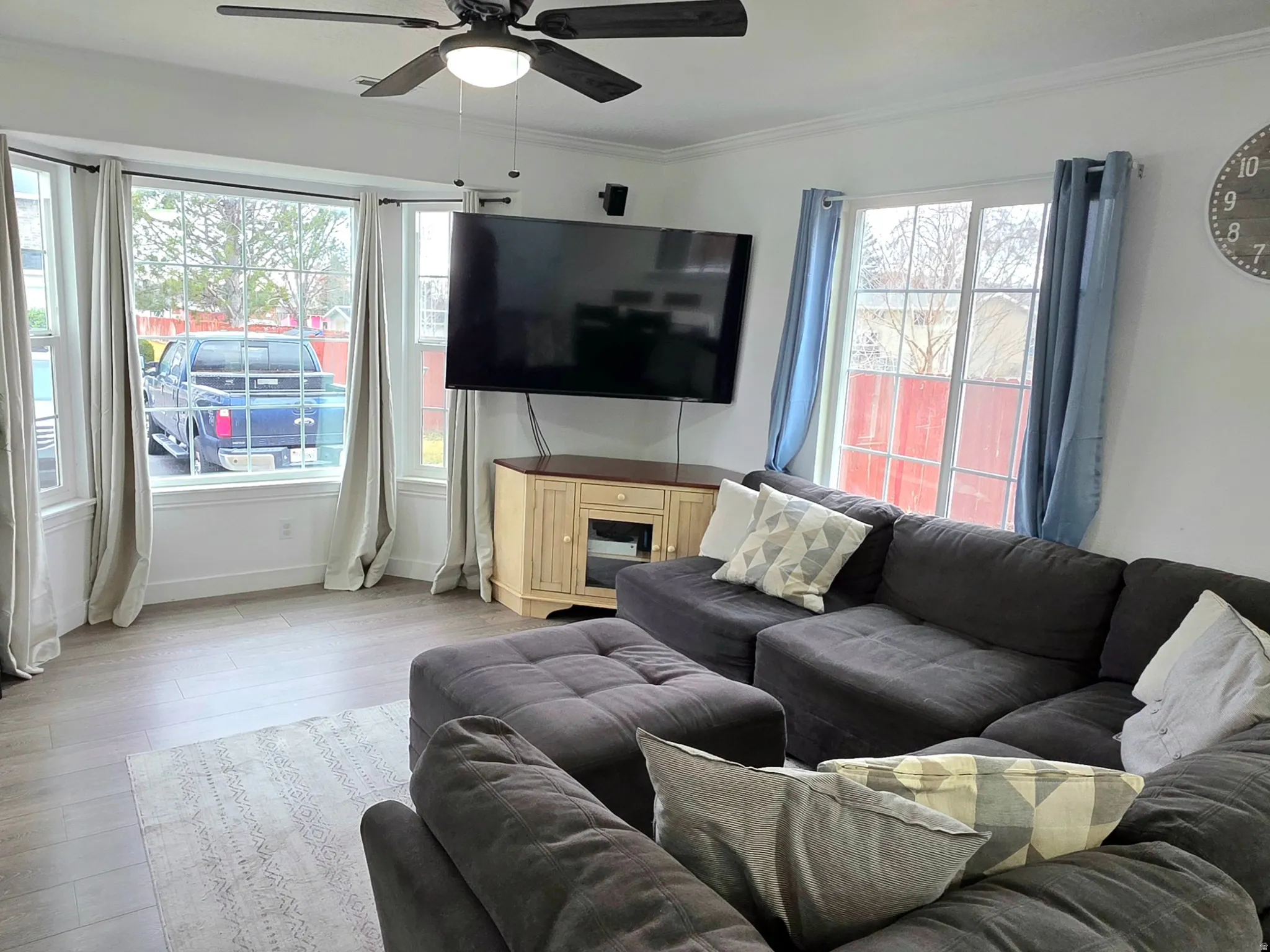 Living area with light wood-type flooring, ornamental molding, and ceiling fan