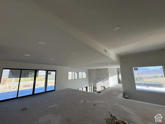 Recessed ceiling lighting, large sliding glass doors, multiple large windows, stone-clad fireplace, and a partial open-concept design