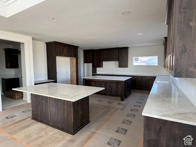 Spacious kitchen featuring two large islands with light-toned countertops, extensive dark wood cabinetry, and recessed lighting