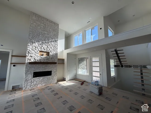 Stacked stone fireplace with a wood mantel, high ceilings, large windows, and a floating staircase