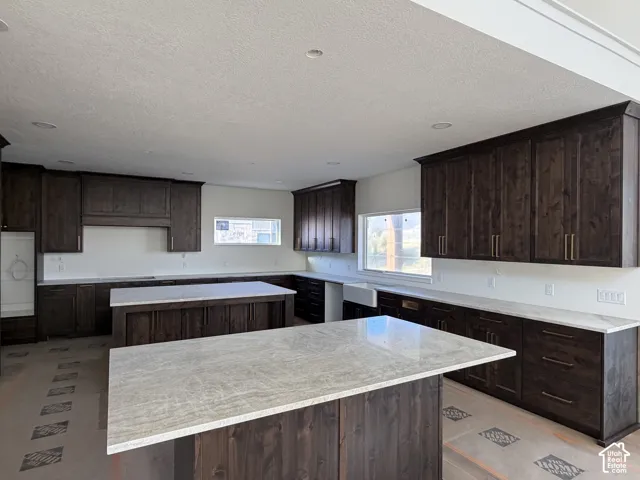 Kitchen featuring two central islands with stone countertops, dark wood-finish cabinetry, a farmhouse-style sink, and recessed lighting