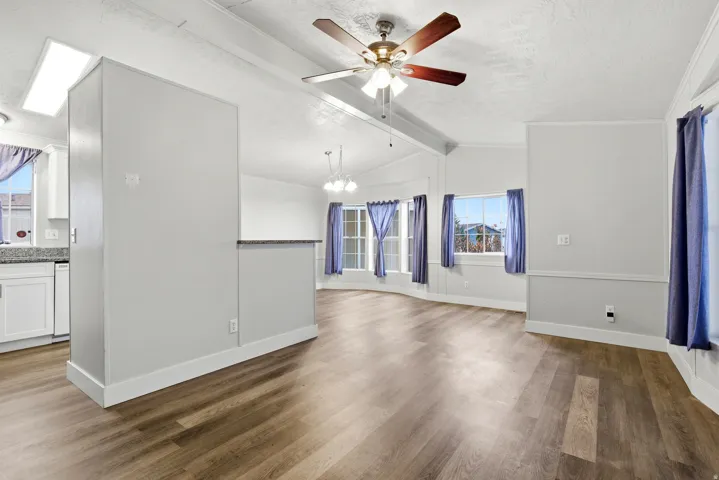 Unfurnished living room featuring wood finished floors, beamed ceiling, ceiling fan, and a chandelier