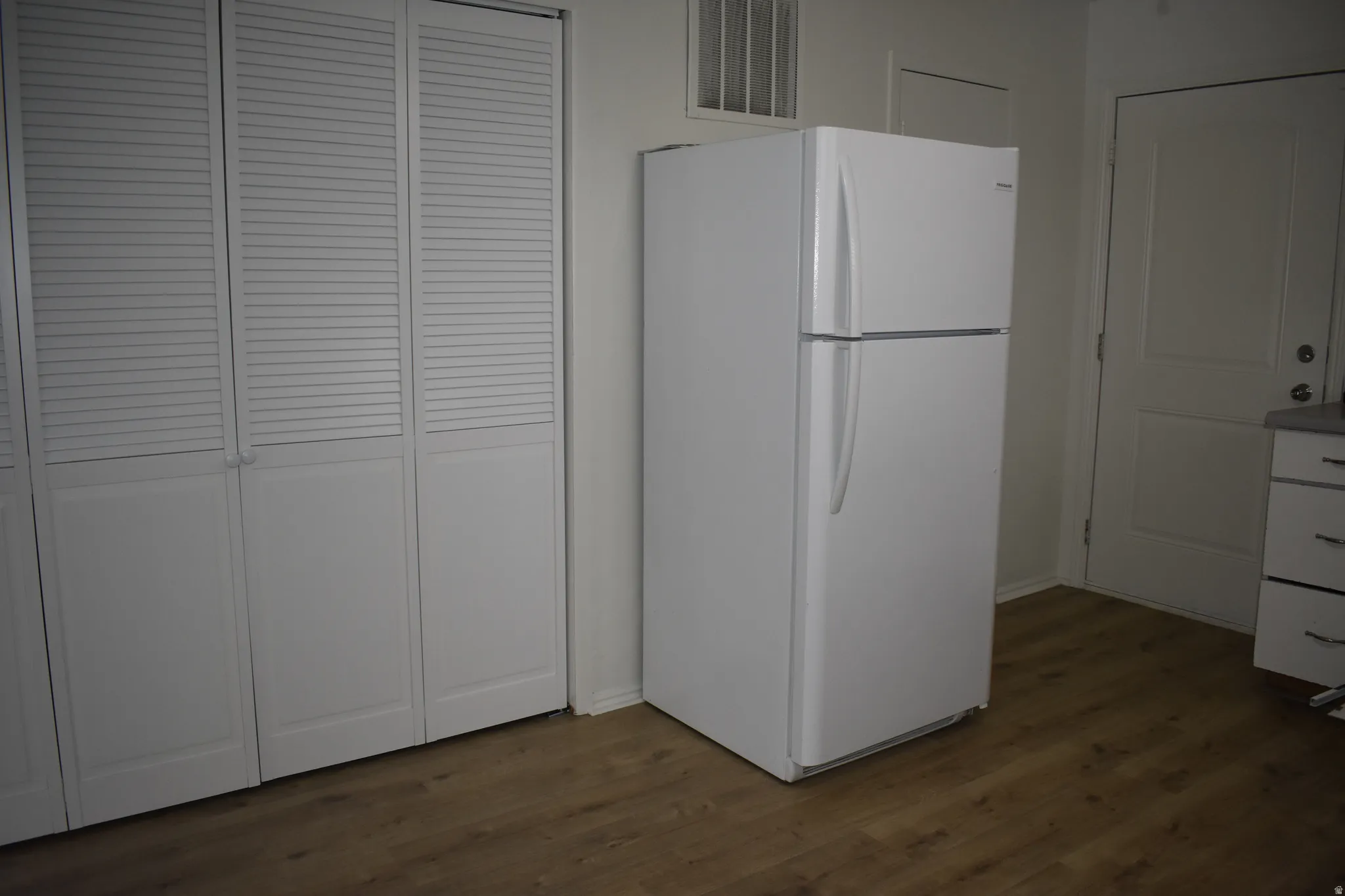Kitchen with freestanding refrigerator, dark wood-style floors, and white cabinetry