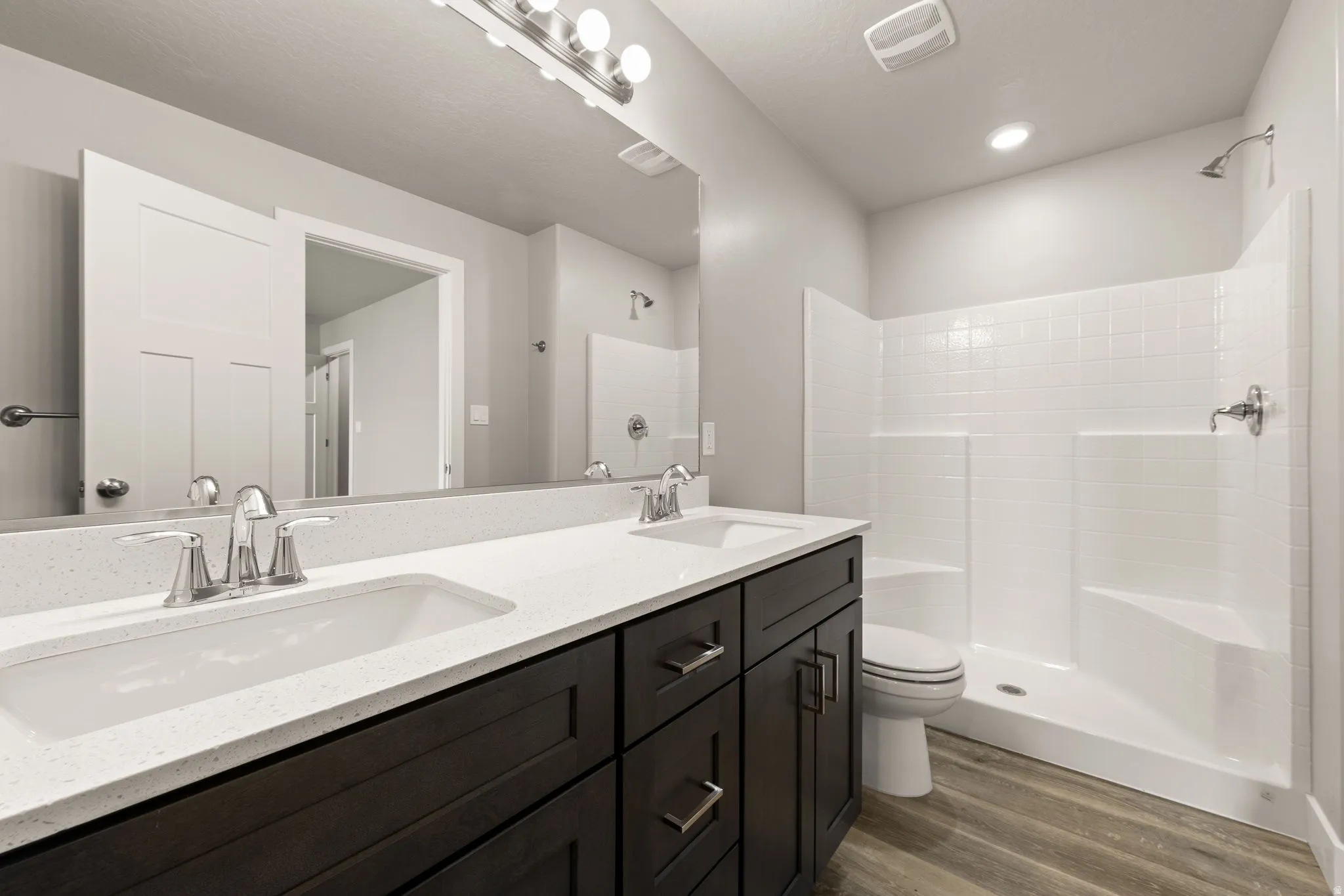 Bathroom with double vanity, dark wood-style floors, and a shower stall