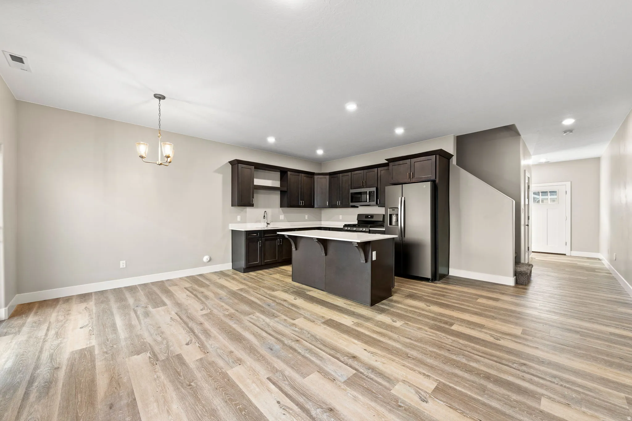 Kitchen featuring dark wood finish cabinets, a breakfast bar, stainless steel appliances, suspended lighting, and light wood-type flooring