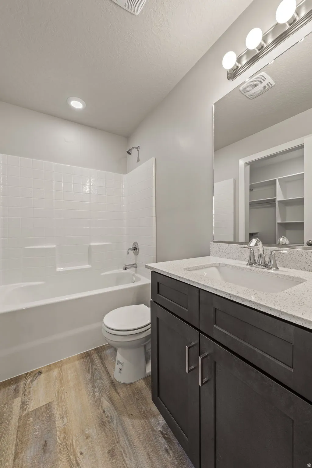 Bathroom with shower / tub combination, light wood-style floors, vanity, and a textured ceiling