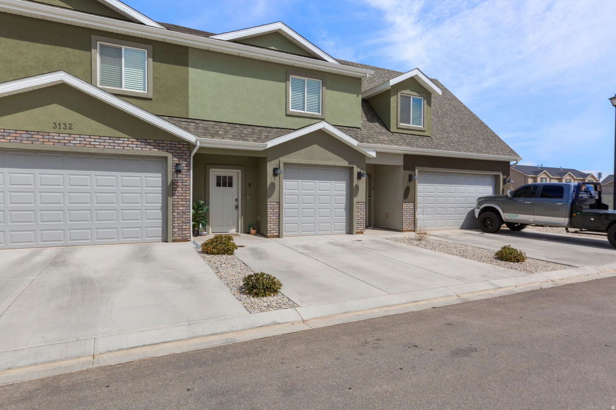 Traditional home featuring stucco siding, roof with shingles, brick siding, driveway, and an attached garage
