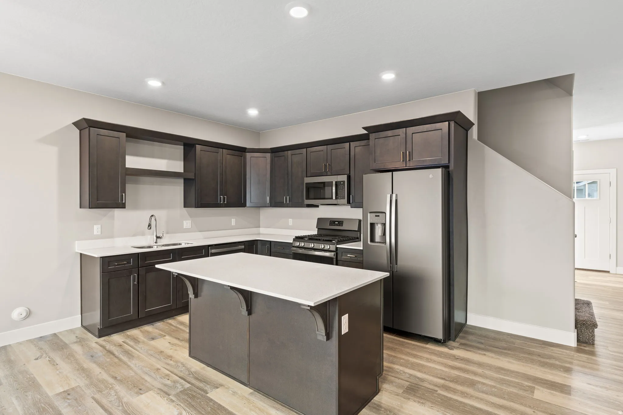Kitchen with dark wood finish cabinets, stainless steel appliances, a kitchen bar, a center island, and recessed lighting
