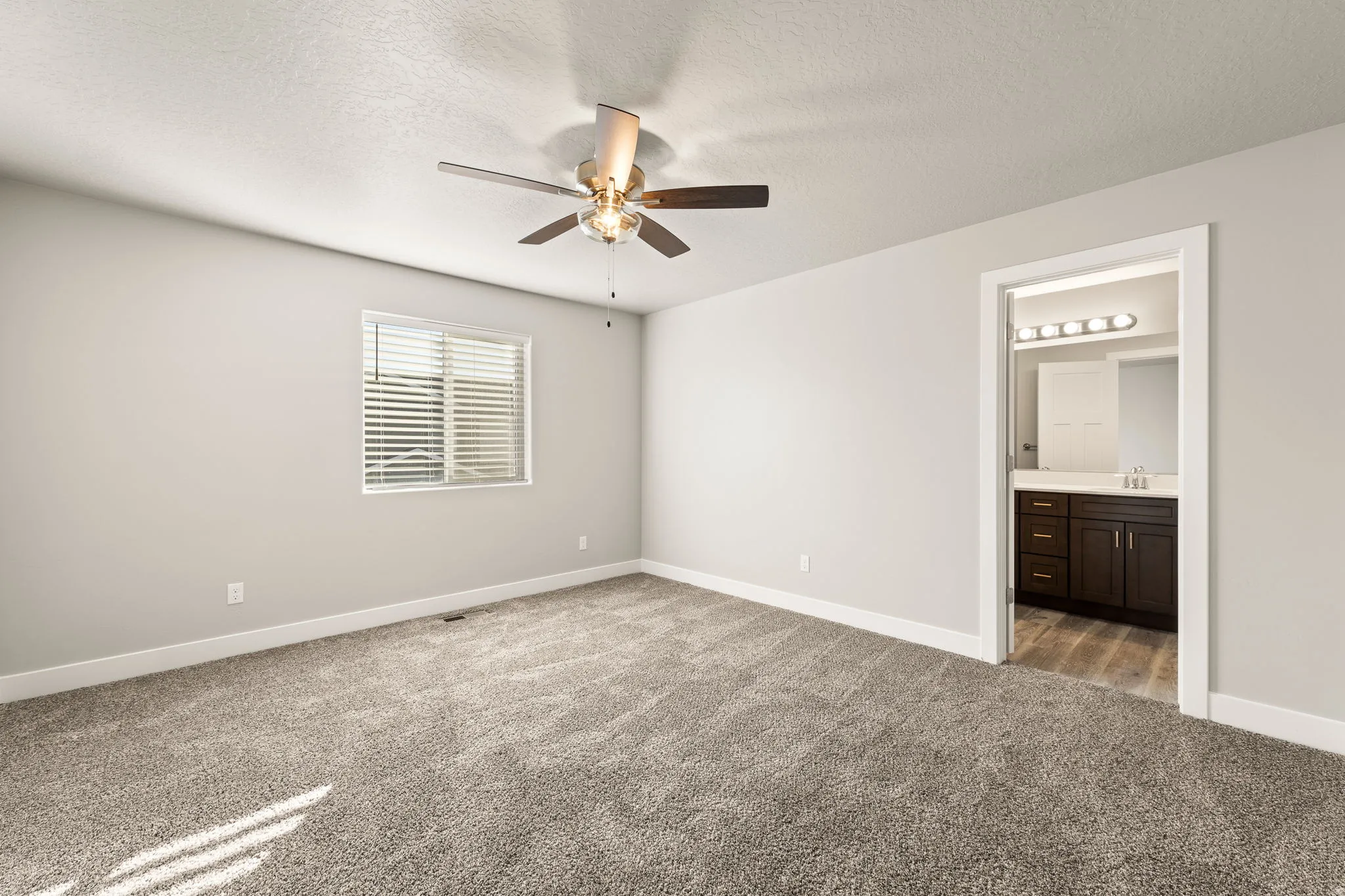 Unfurnished bedroom with light carpet, a ceiling fan, a textured ceiling, and ensuite bathroom