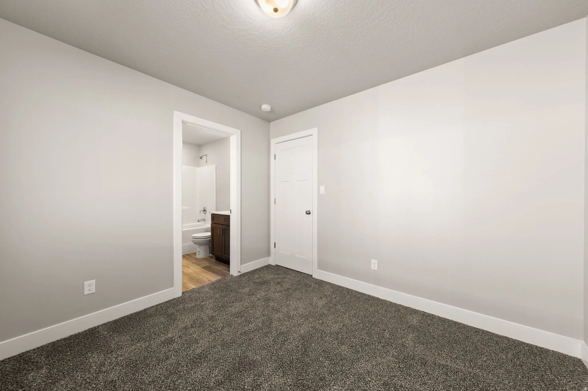 Unfurnished bedroom featuring carpet flooring, ensuite bathroom, and a textured ceiling
