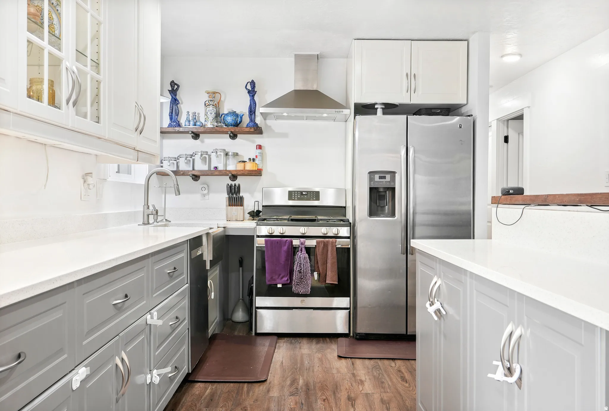 Kitchen with open shelves, stainless steel appliances, light stone countertops, dark wood-style floors, and white cabinetry