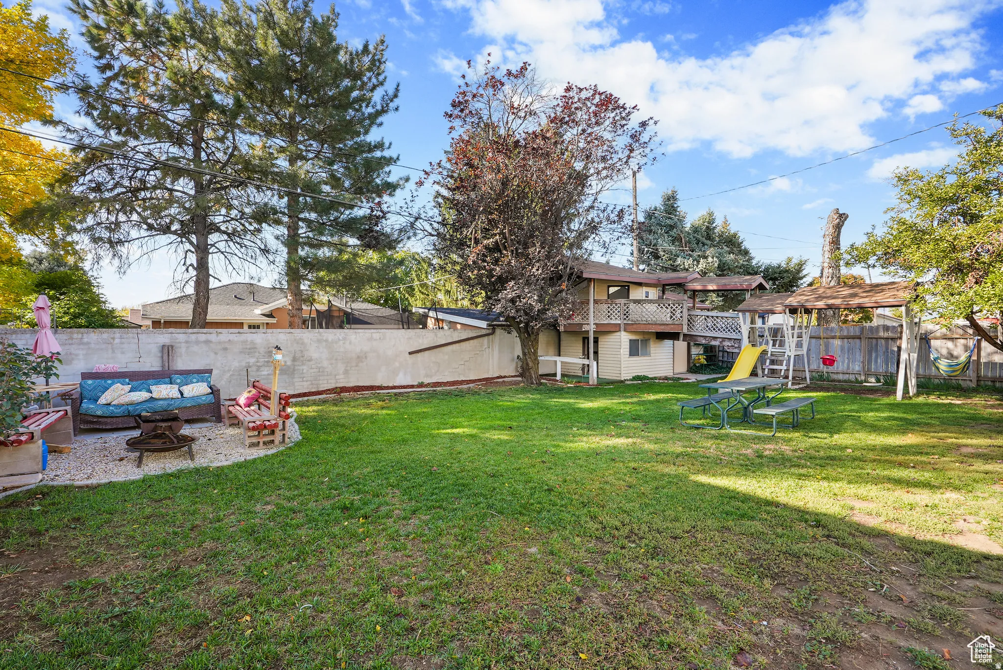 Fenced backyard with a playground, a patio, and an outdoor living space with a fire pit