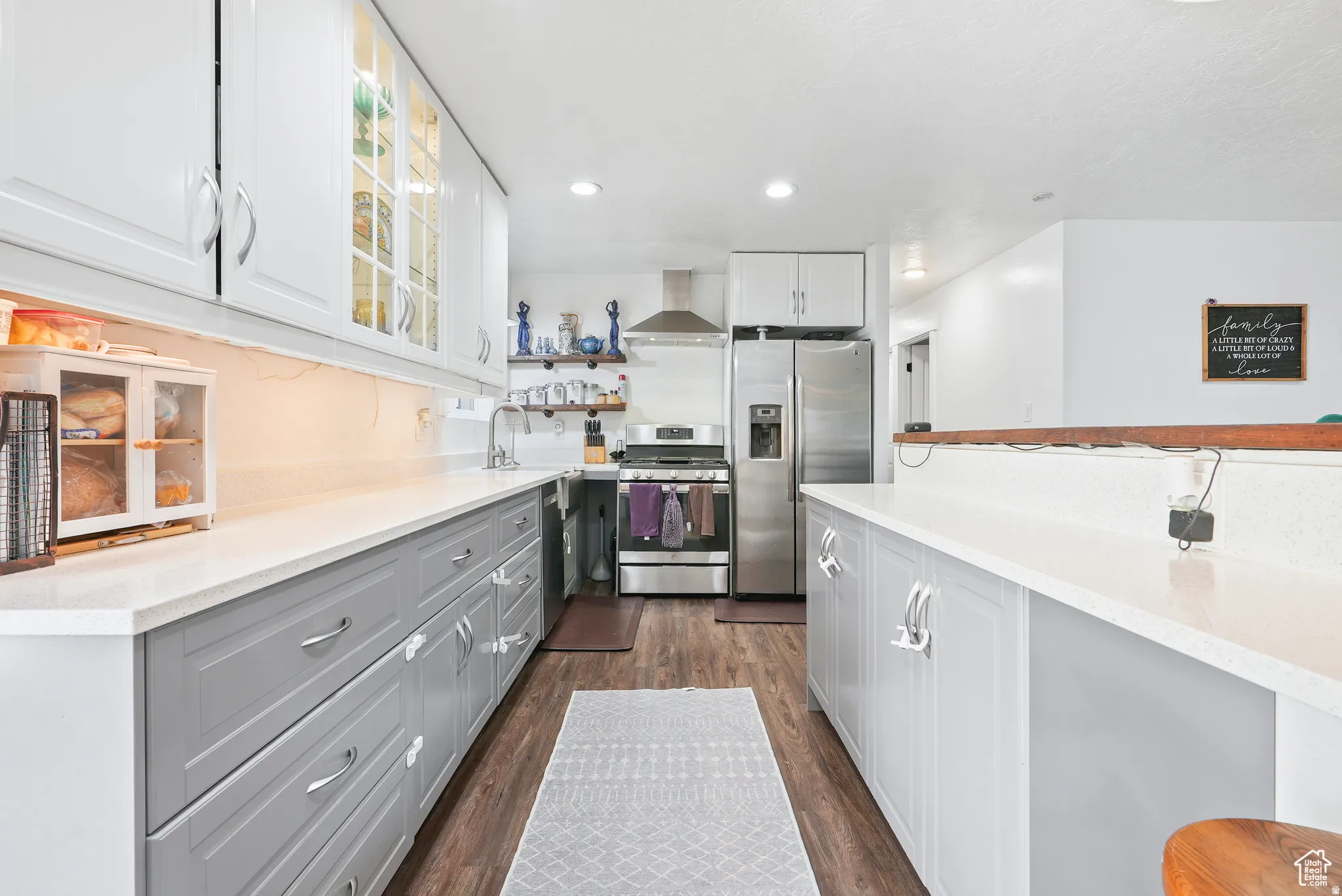 Kitchen featuring two tone color scheme, stainless steel appliances, open shelves, light stone counters, and glass insert cabinets