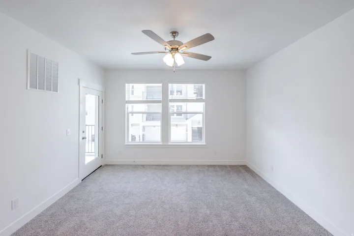 Textured carpeting, multiple windows, ceiling fan with integrated lighting, white trim, and a glass-paneled door