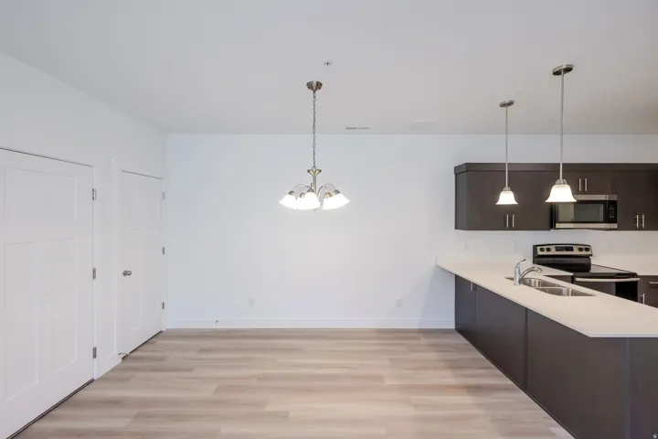 Wood-finish flooring throughout, brushed nickel chandelier, recessed lighting, dark wood-finish cabinetry, and stainless steel appliances
