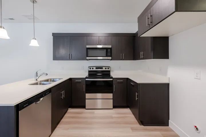 Modern kitchen featuring dark wood-finish cabinetry, stainless steel appliances, light-toned countertops, and wood-finish flooring