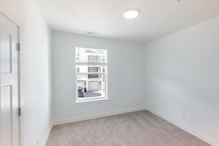 Neutral-toned carpeting, white walls, and a window with horizontal blinds