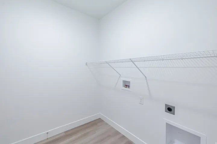Dedicated laundry area featuring a wire storage shelf, utility hookups, and wood-finish flooring