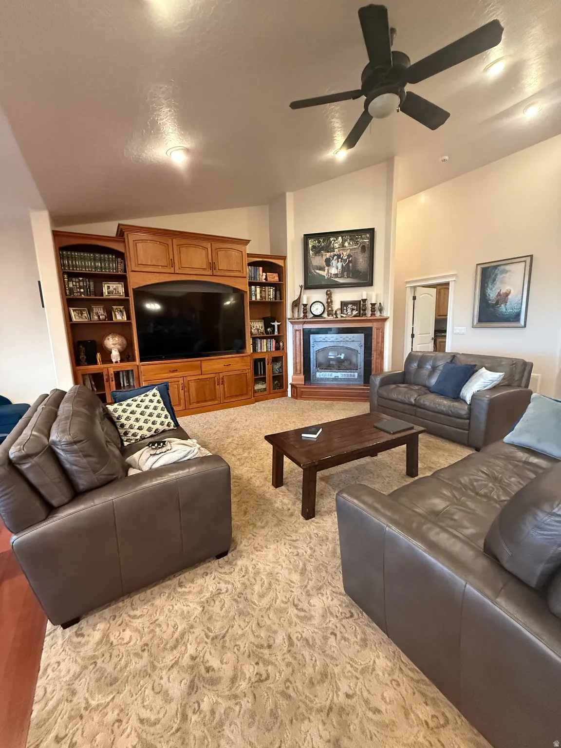 Living room with a ceiling fan, vaulted ceiling, a fireplace, and light carpet