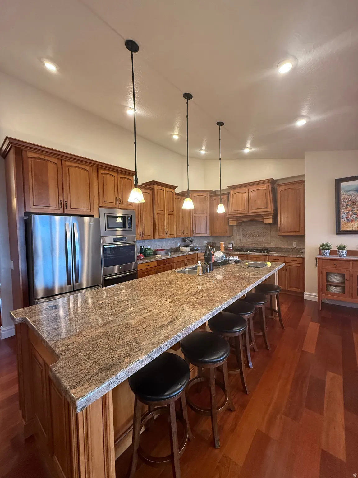 Kitchen with wood finish cabinets, a large island, dark stone counters, pendant lighting, and tasteful backsplash
