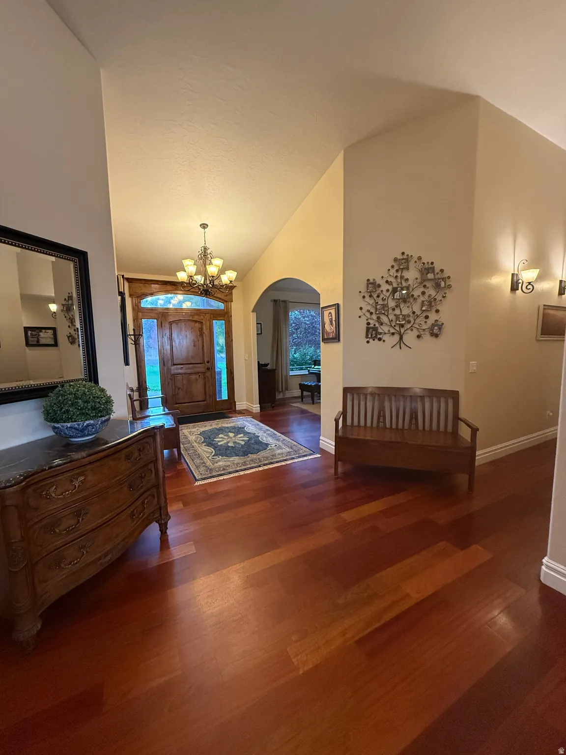 Entrance foyer featuring arched walkways, dark wood-type flooring, a chandelier, and lofted ceiling