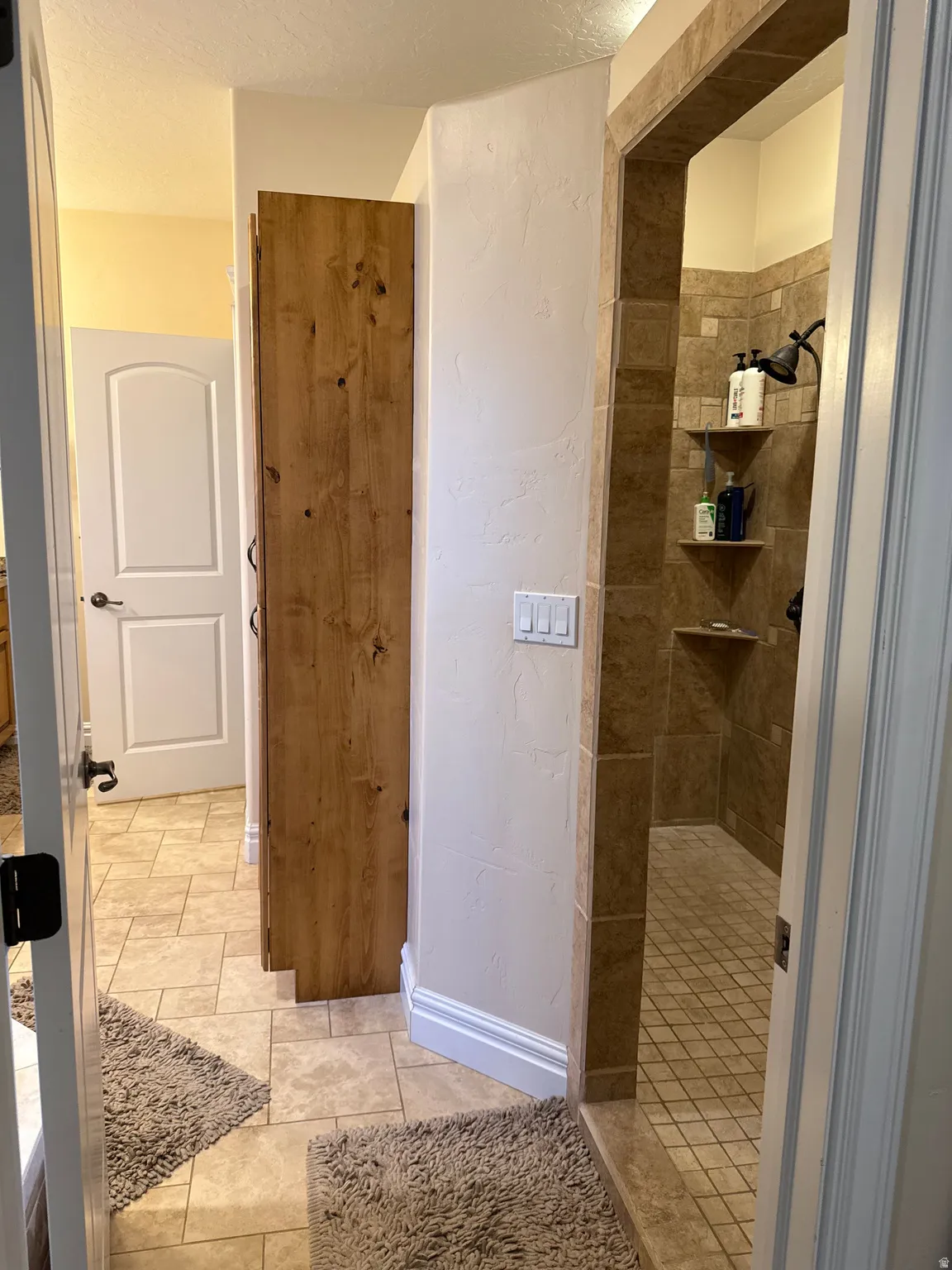 Bathroom with a tile shower, a textured wall, light tile patterned flooring, and a textured ceiling